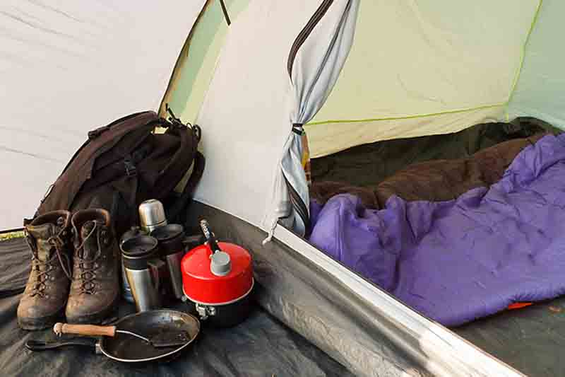 Interior view of a tent set up with various equipment and sleeping bag inside inner compartment, and gear in the vestibule, showing a well organized camp.