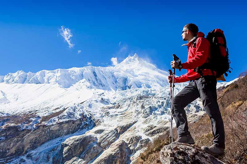 A horizontal image a man hiking in the mountains pictured on a blue sky background.