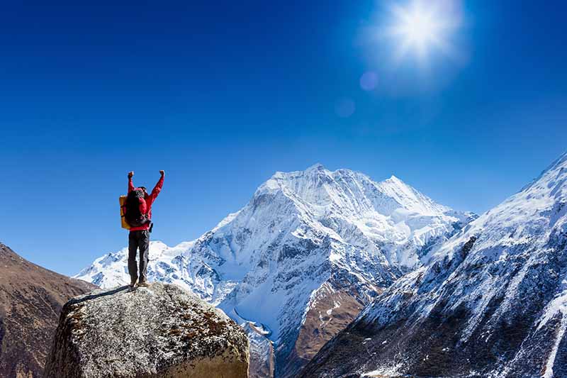 A horizontal image of a hiker with snow-capped mountains, with a blue sky background.