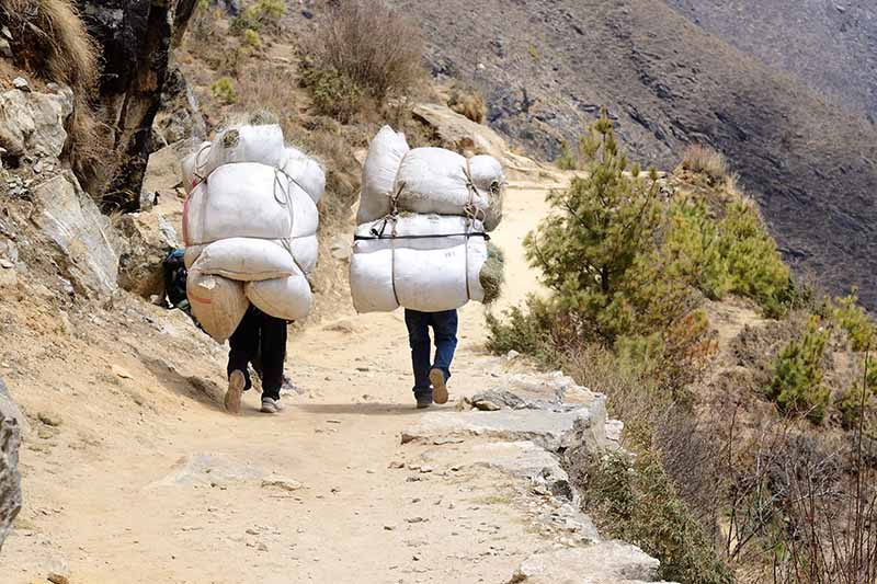 A close up horizontal image of two sherpas trekking in Nepal carrying heavy loads.