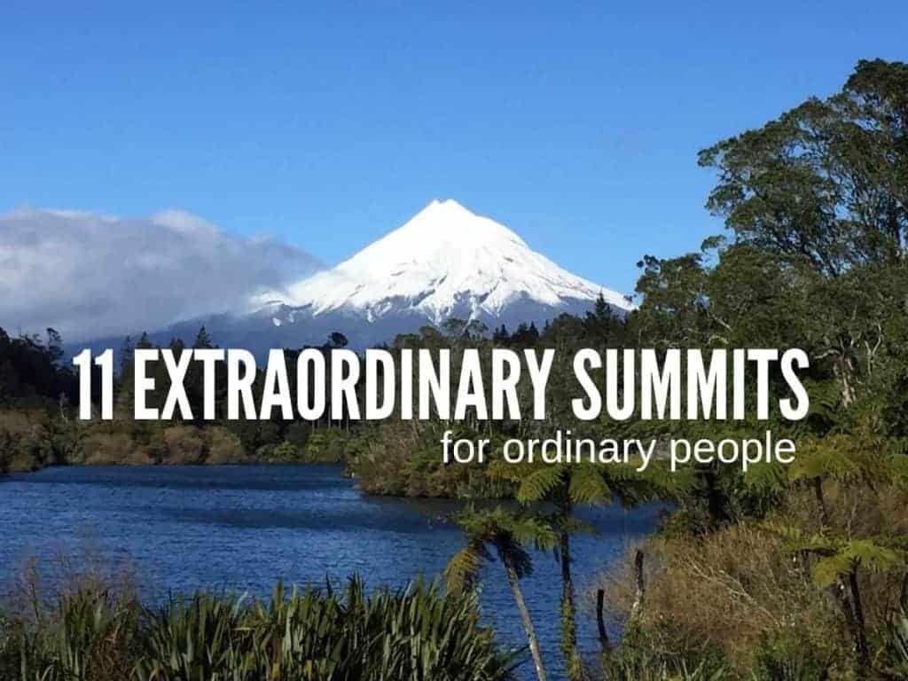 A view of Mt. Taranaki, New Zealand, across a small lake with the snow capped peak visible in the distance against a bright blue sky. In the center of the frame is white text.